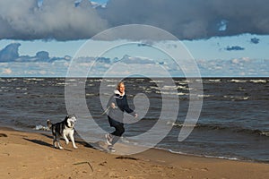 A girl runs with a husky dog Ã¢â¬â¹Ã¢â¬â¹on the beach on a windy autumn day